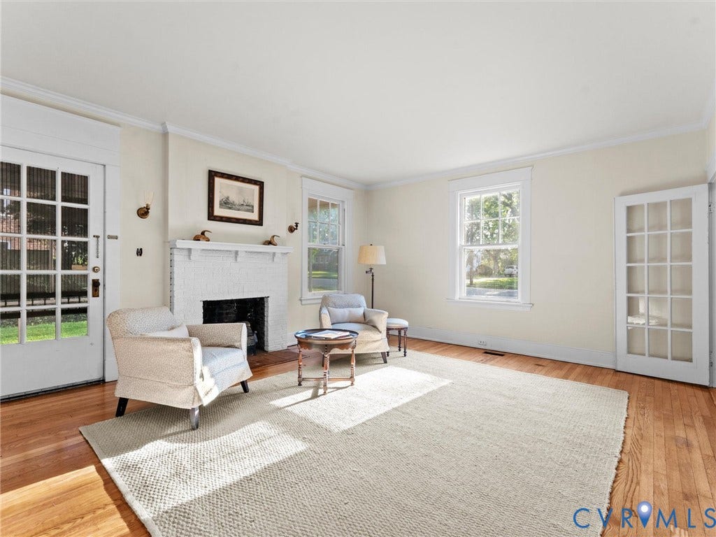 Bright, light-filled living room featuring hardwood flooring, a working fireplace with white surround and mantelpiece, multiple multi-pane windows providing natural light, and French doors opening to outdoor spaces