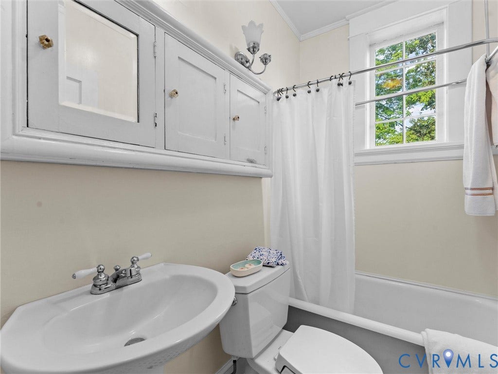 Classic bathroom featuring a pedestal sink with chrome faucet, white subway tile wainscoting, mirrored medicine cabinet with sconce lighting, and a bathtub with white tile surround and curtain rod