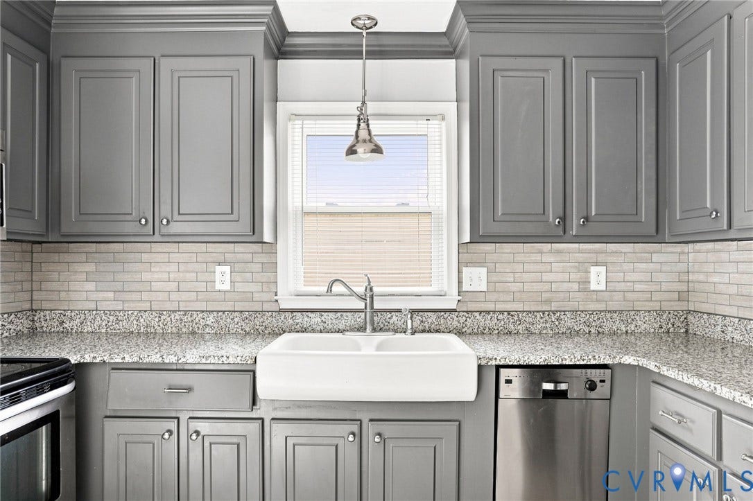 Gray shaker-style cabinetry, white farmhouse sink, stainless steel dishwasher, speckled countertops, and a subway tile backsplash