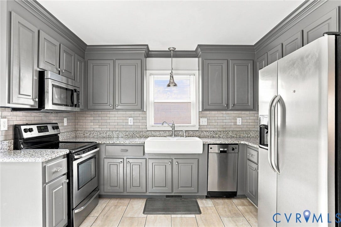 Kitchen featuring grey shaker-style cabinetry, stainless steel appliances, a white farmhouse sink, and light-toned tile flooring