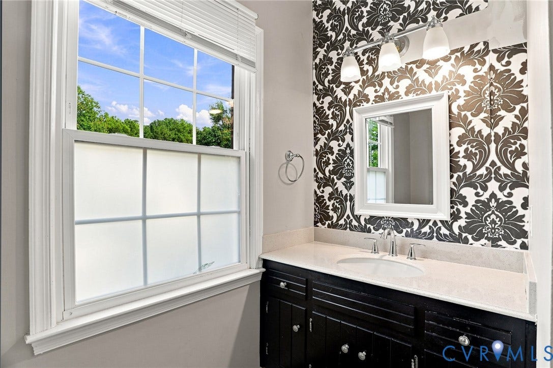 White framed window, black vanity with silver hardware, single undermount sink, countertop, and patterned accent wall
