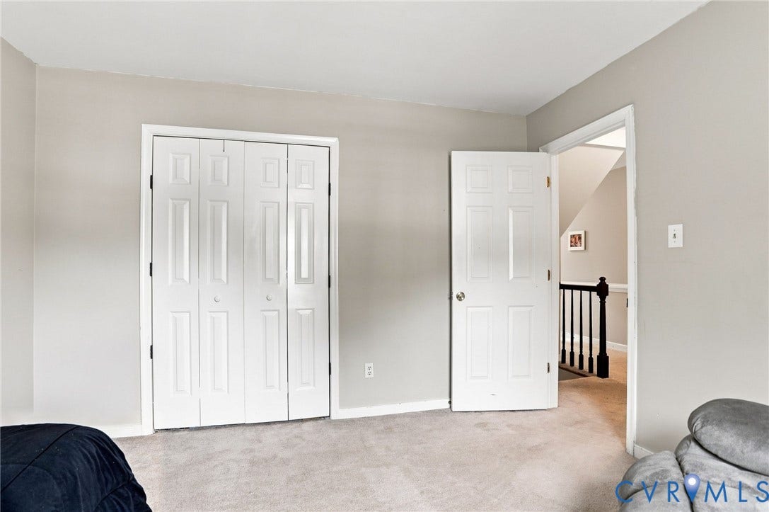 Neutral wall paint, light-toned carpet flooring, white bi-fold closet doors, white paneled interior door, and dark wood-finish banister