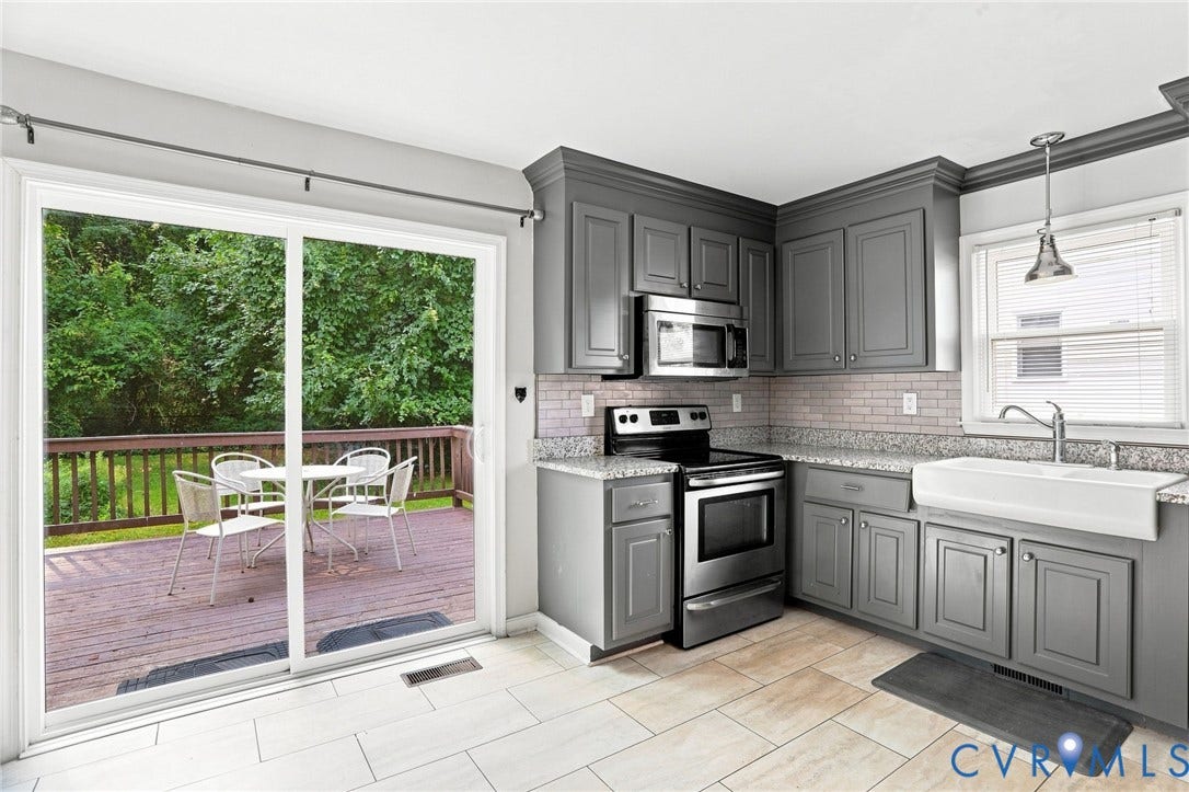 Kitchen featuring gray shaker-style cabinetry, stainless steel appliances, light-toned tile flooring, granite countertops, and a white farmhouse sink