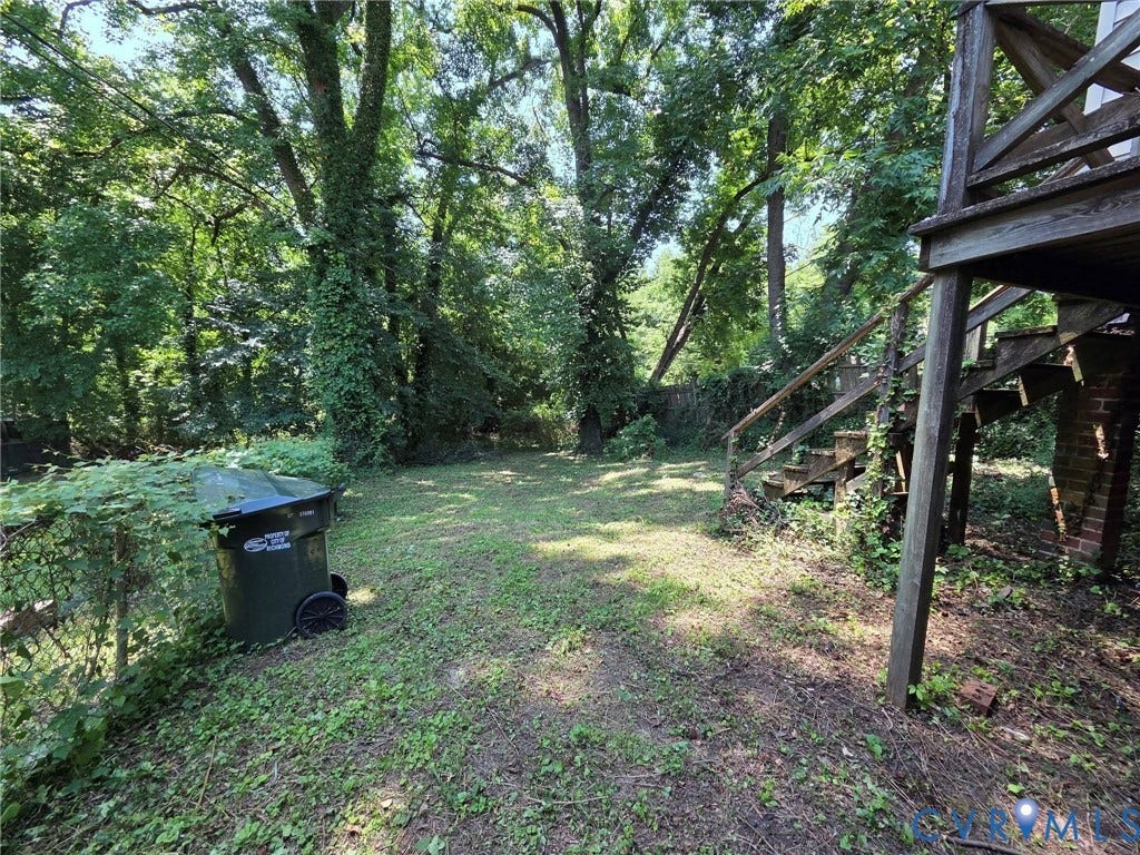 Expansive backyard with a mix of grass and natural ground cover, mature trees, and a wooden deck with stairs