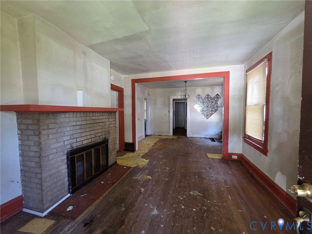 Brick fireplace with a red-painted mantel, wood-finish flooring, and an architectural doorway