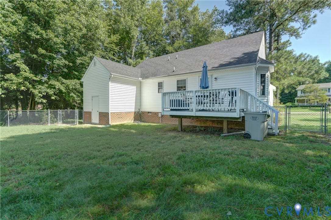4229 Greenbriar Drive, Chester, VA 23831 Expansive grass lawn, white siding exterior, elevated wood deck with railing, chain-link fence, and an attached storage shed with brick foundation