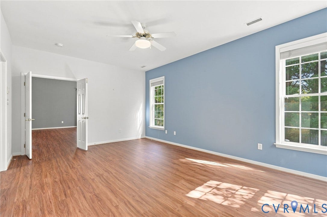 Spacious room featuring wood-finish flooring, multiple windows, a ceiling fan, and French doors
