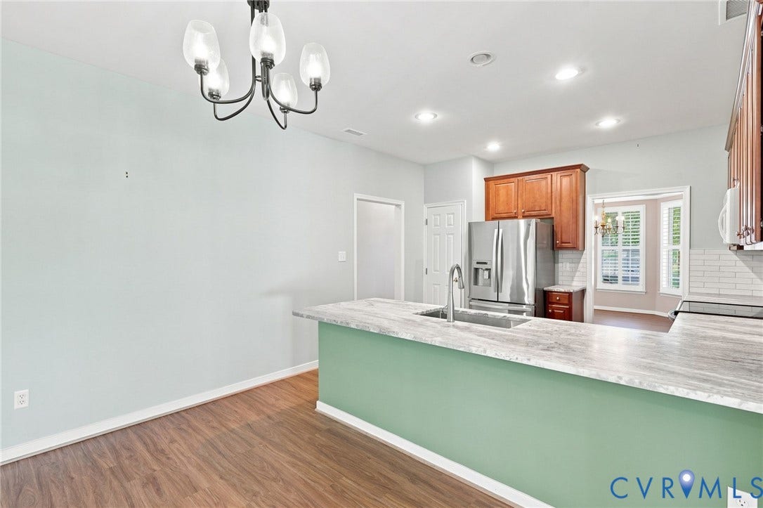 Wood-finish flooring, recessed lighting, chandelier, kitchen island with sink, and stainless steel appliances