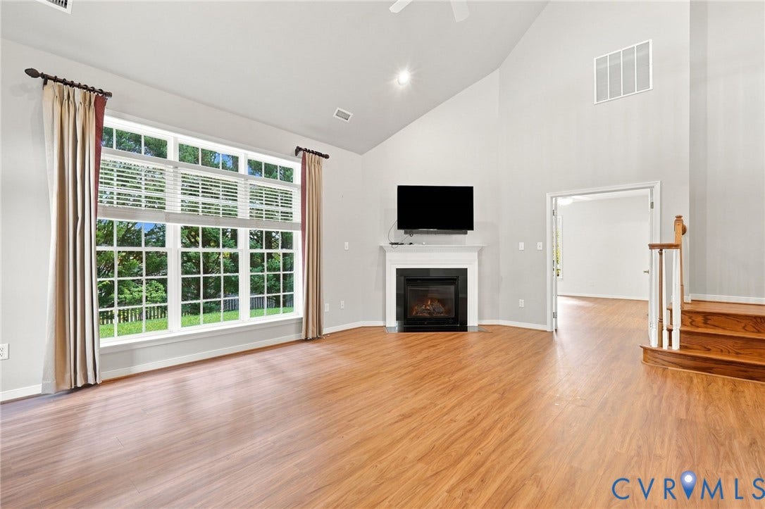 Vaulted ceiling, wood-finish flooring, large multi-pane window, gas fireplace with white mantel, wood staircase with white balusters