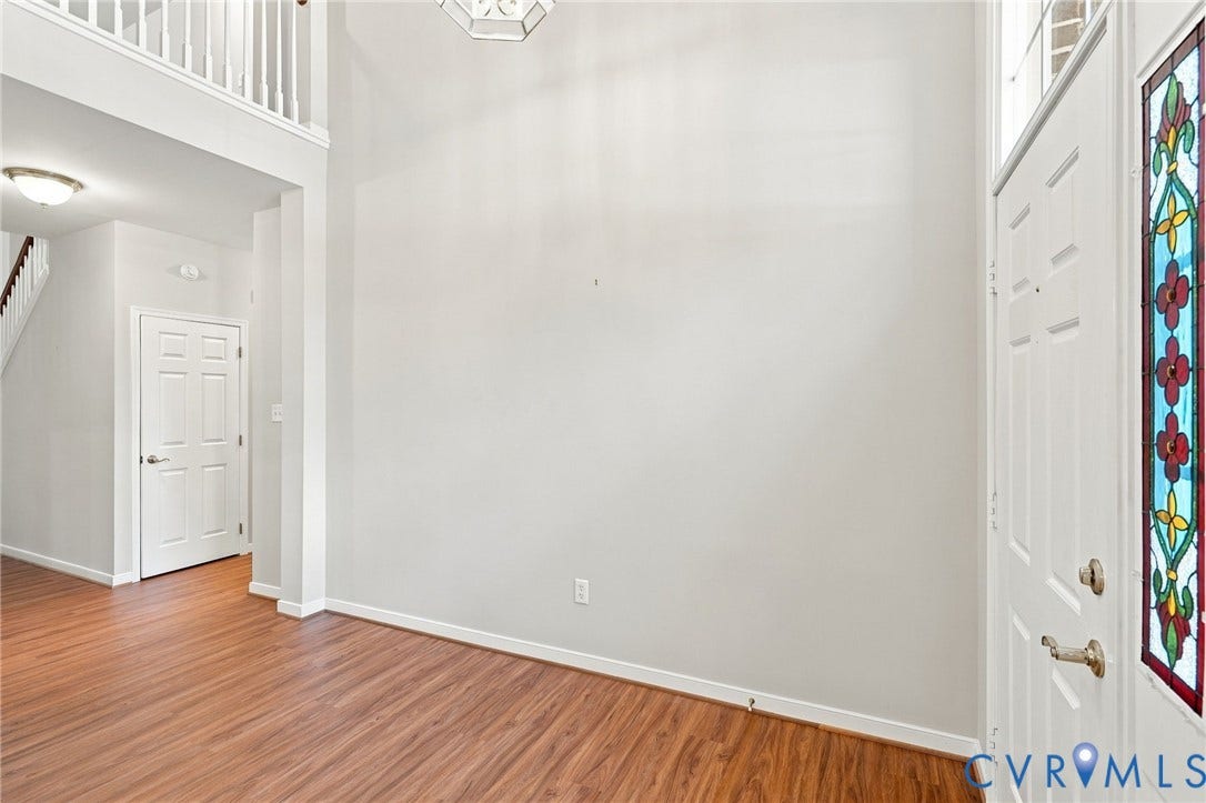 Entryway featuring wood-finish flooring, a white front door with stained glass insert, and a two-story ceiling with an overhead light fixture