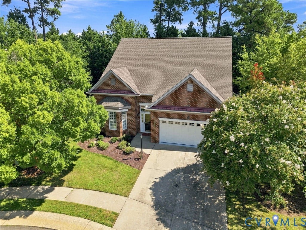 Brick exterior, bay window, attached garage, concrete driveway, and mature landscaping
