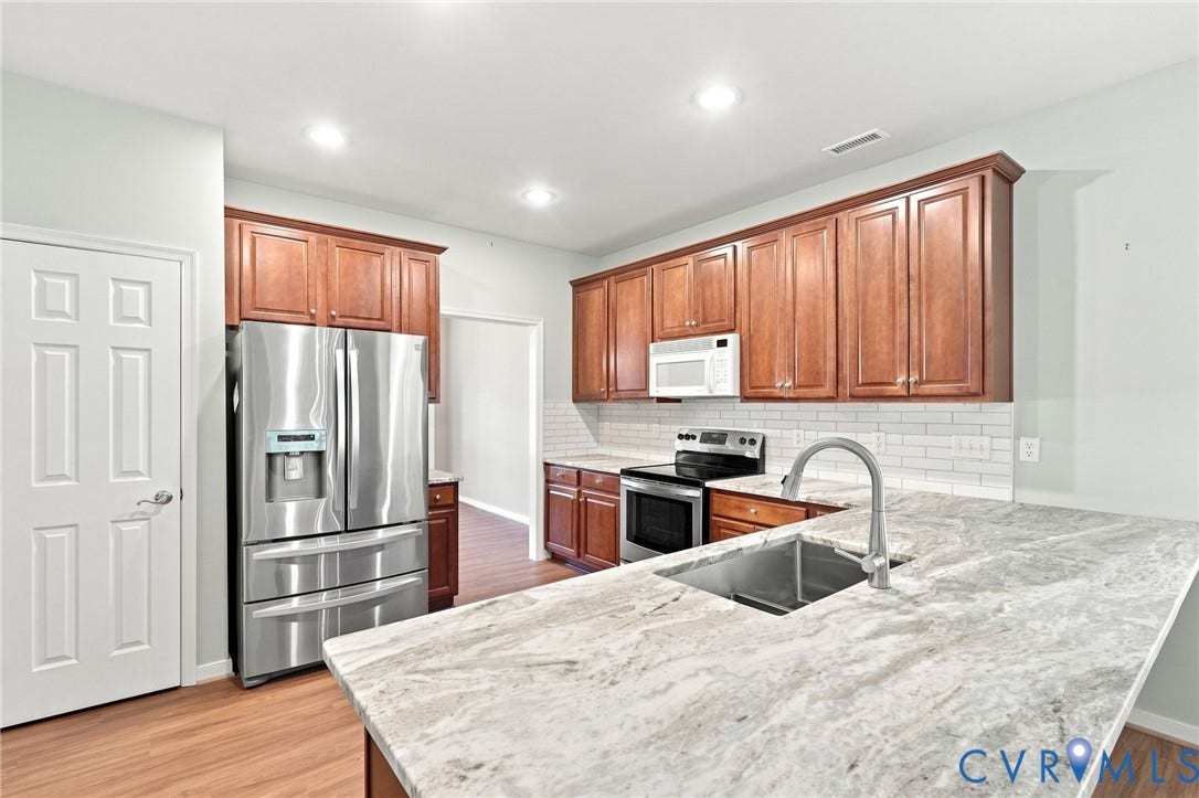 Expansive kitchen featuring wood-finish flooring, recessed lighting, wood cabinetry, a stainless steel sink with a gooseneck faucet, and a large countertop