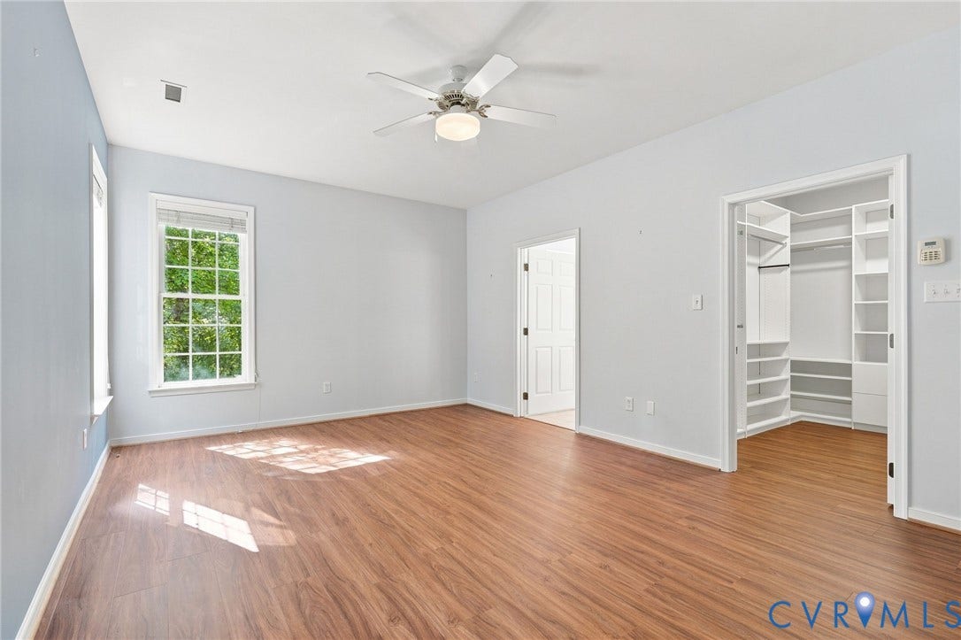 Spacious room featuring wood-finish flooring, multiple windows, a ceiling fan with integrated lighting, and a built-in closet system