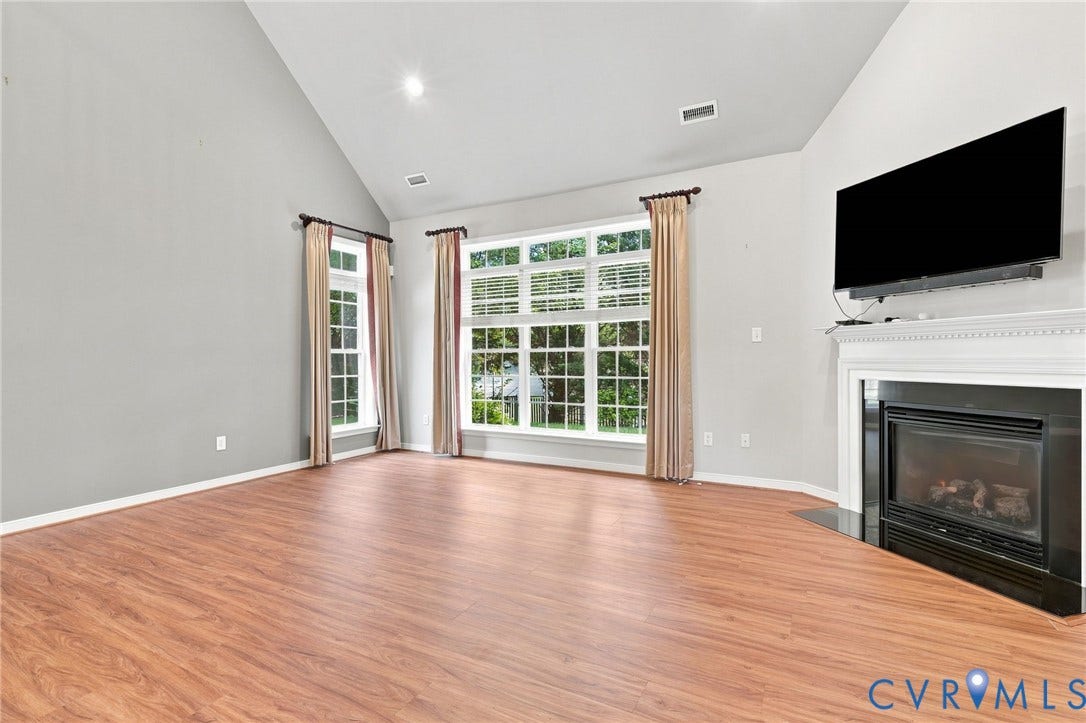 Vaulted ceilings, wood-finish flooring, and a built-in fireplace with a white mantel and black surround