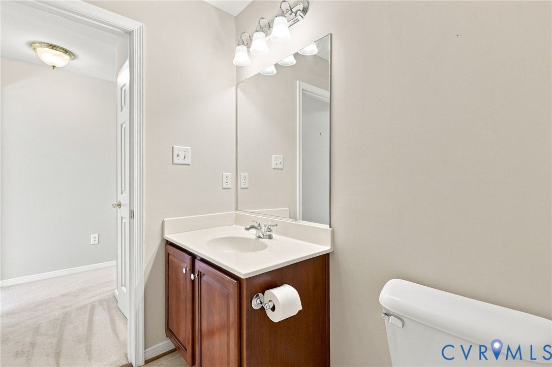 Vanity with a light-colored countertop and integrated sink, wood-finish cabinetry with silver-tone hardware, and an overhead vanity light fixture