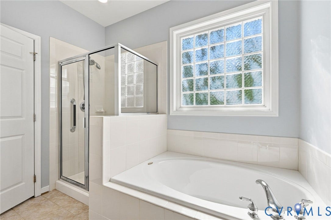 White tiled surround soaking tub with chrome fixtures, glass block window, and a separate glass-enclosed shower