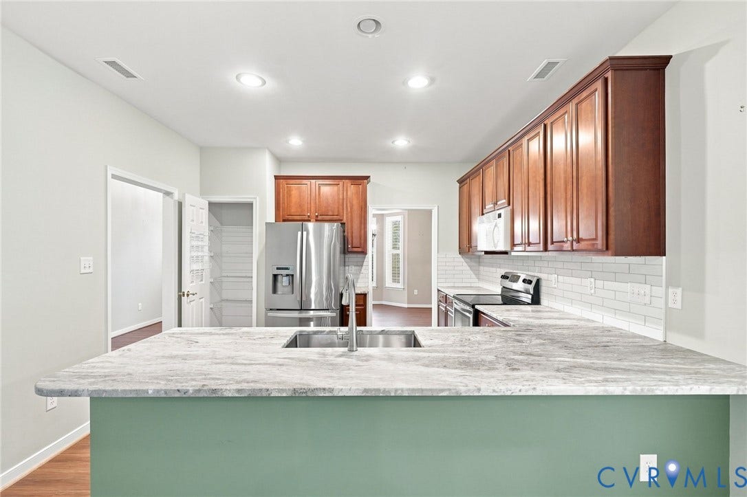 Kitchen featuring a large island with an undermount sink, stainless steel appliances, wood-finish cabinetry, and a white subway tile backsplash