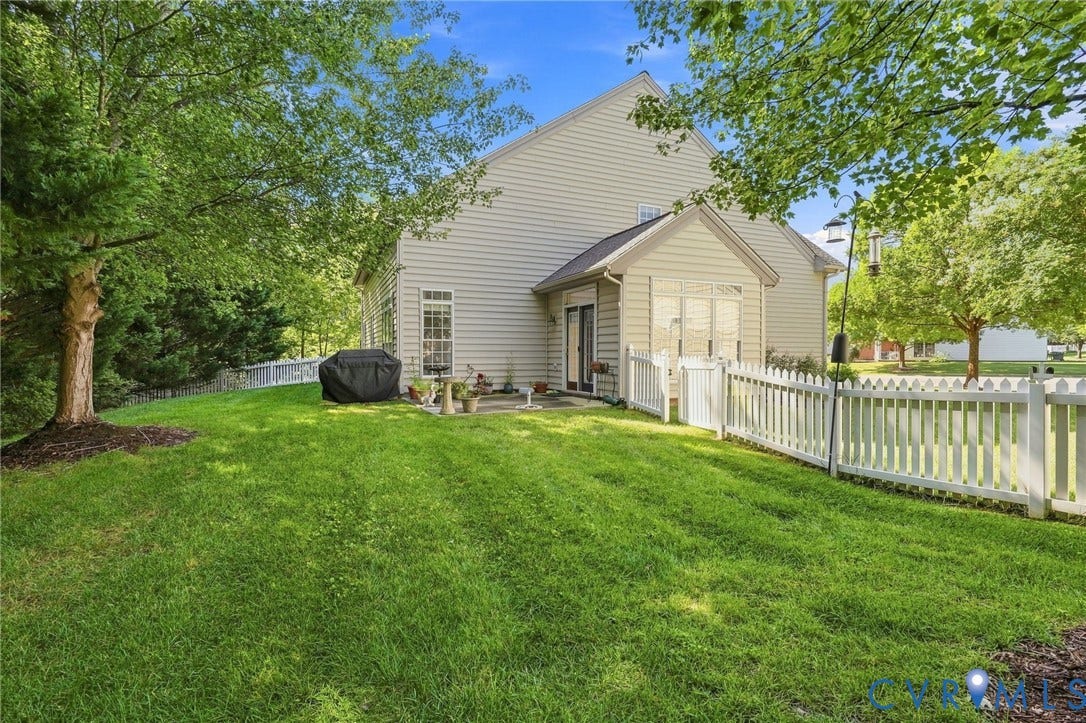 Expansive green lawn, white picket fence, mature trees, and a patio area
