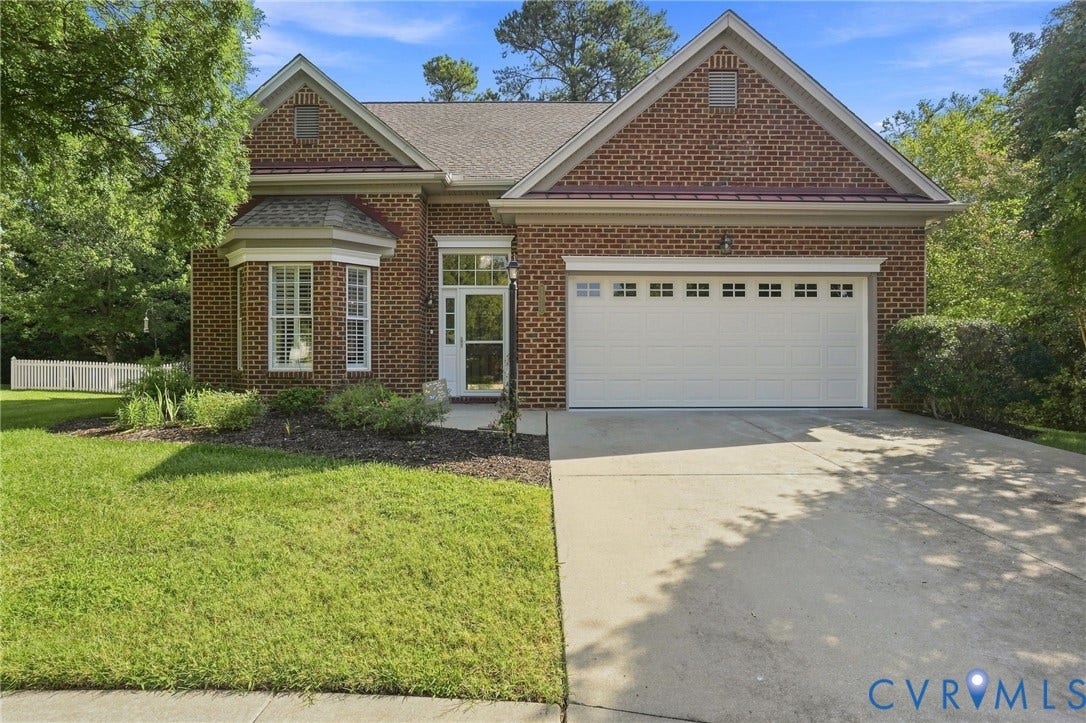 Brick exterior with a dormer, bay window with shutters, white entry door with full-light storm door, and an attached two-car garage
