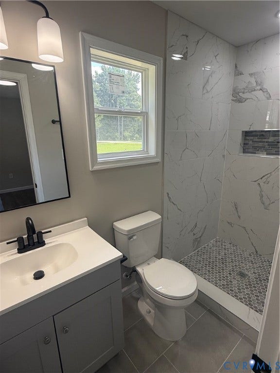 3430 The Loop Rd, Glendale, Montross, VA 23231 Bathroom featuring a single vanity with dark hardware, a white countertop, a toilet, a walk-in shower with large format tile and a hexagon mosaic floor, and a window