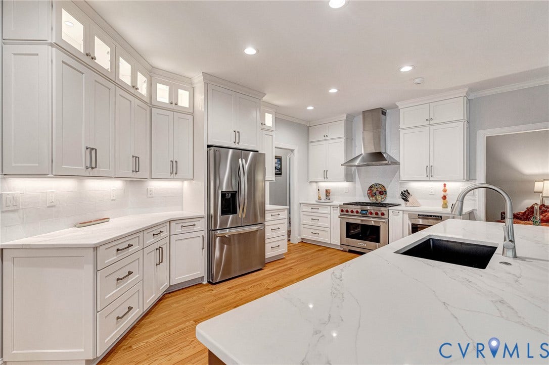 White shaker cabinetry, stainless steel appliances, quartz countertops, wood-finish flooring, and a large center island with an integrated sink