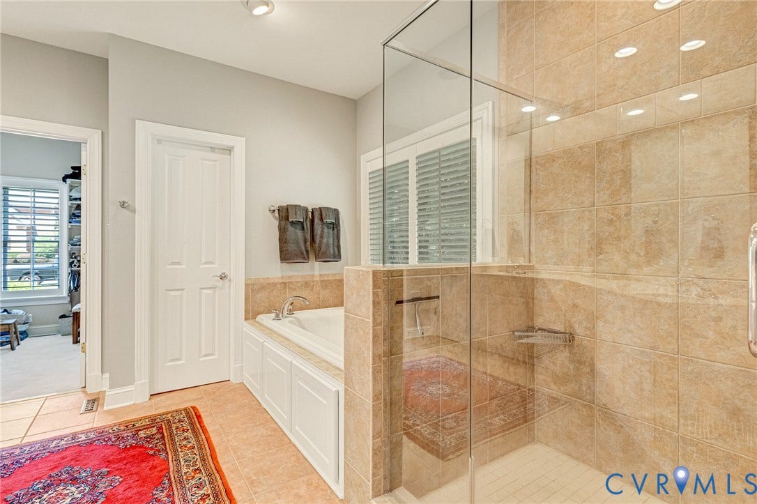 Built-in soaking tub with paneled surround, glass-enclosed shower with tiled walls, and recessed lighting