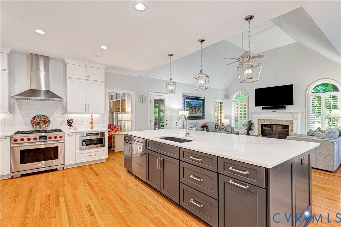 Open-concept kitchen with a large central island, stainless steel appliances, wood-finish flooring, and vaulted ceilings