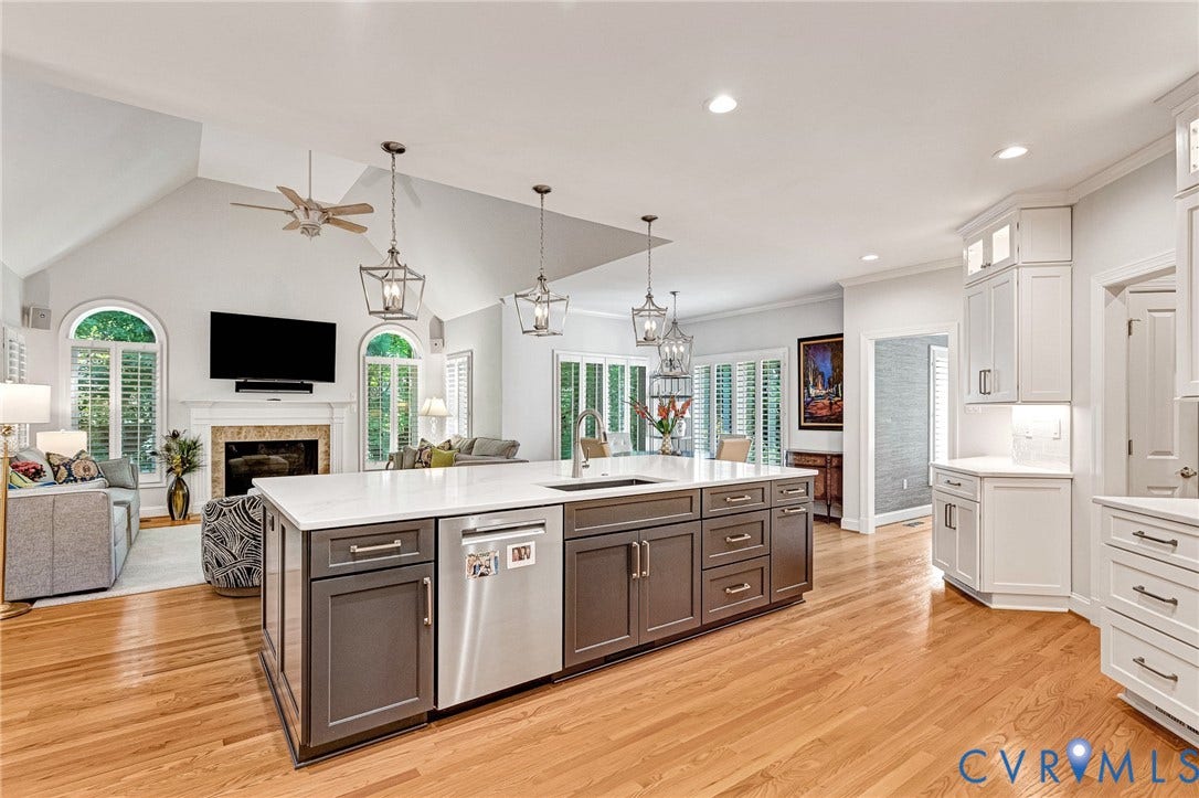 Hardwood flooring throughout, kitchen island with built-in sink and stainless steel dishwasher, white and gray cabinetry, vaulted ceiling with ceiling fan, and fireplace with mantel