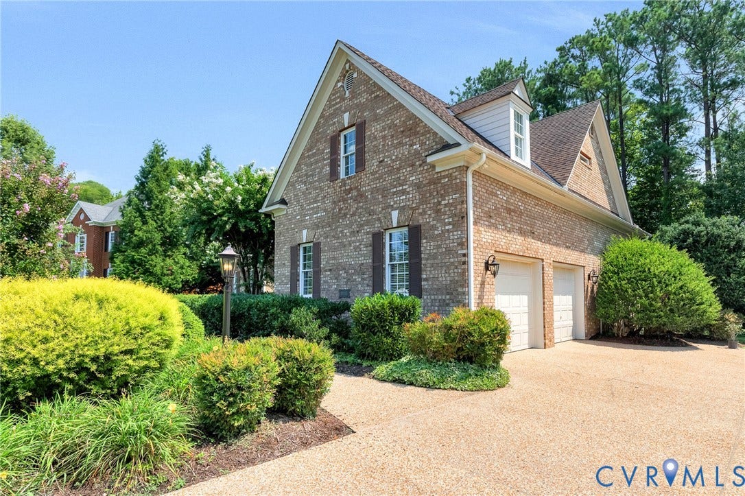 Brick exterior with white trim, two garage doors, dormer window, and established landscaping