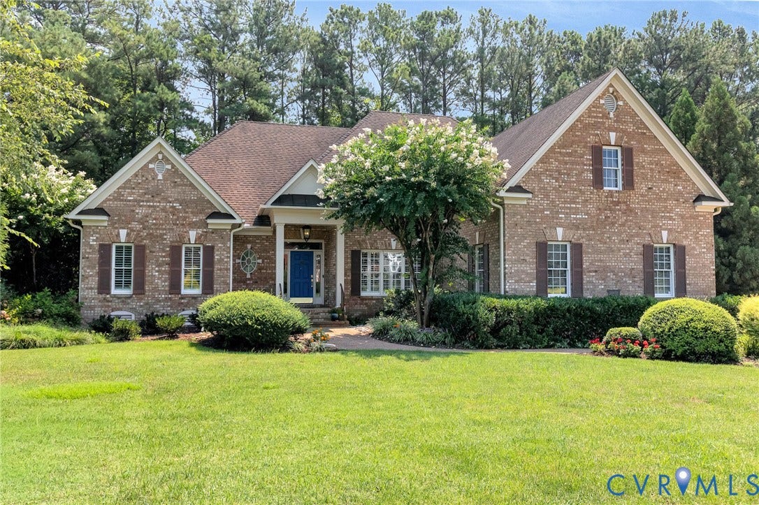 Brick exterior with gabled roof lines, prominent front porch, dark wood shutters, and manicured landscaping