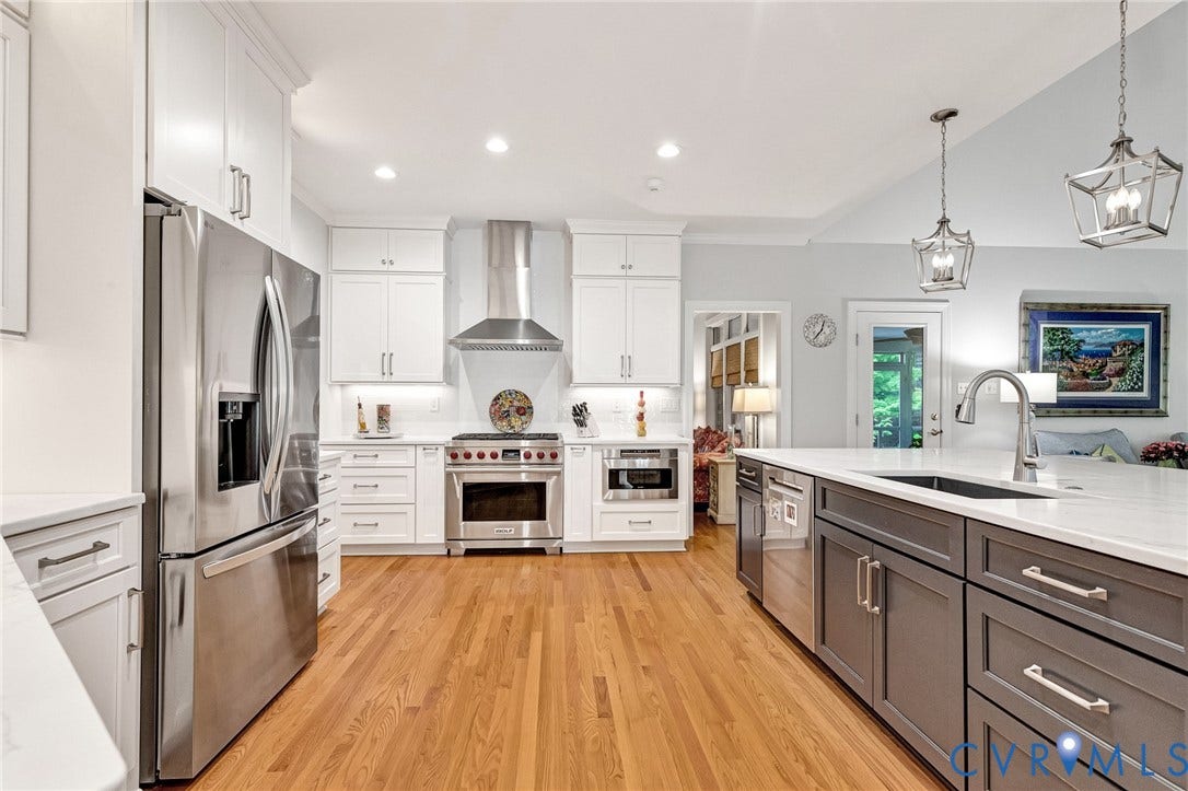 Kitchen featuring wood-finish flooring, white upper and lower cabinetry, stainless steel appliances, a center island with sink, and vaulted ceilings with pendant lighting