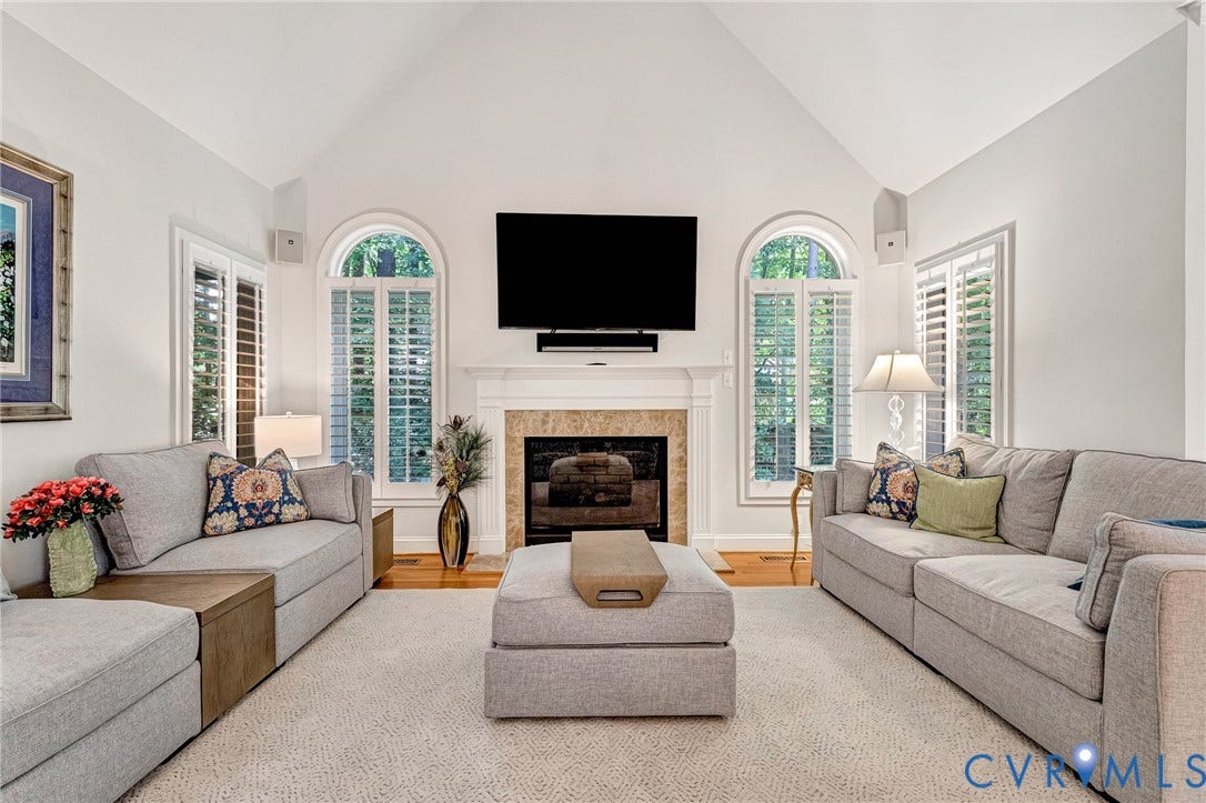 Vaulted ceiling, arched window, fireplace with stone surround, white wood plantation shutters, wood-finish flooring