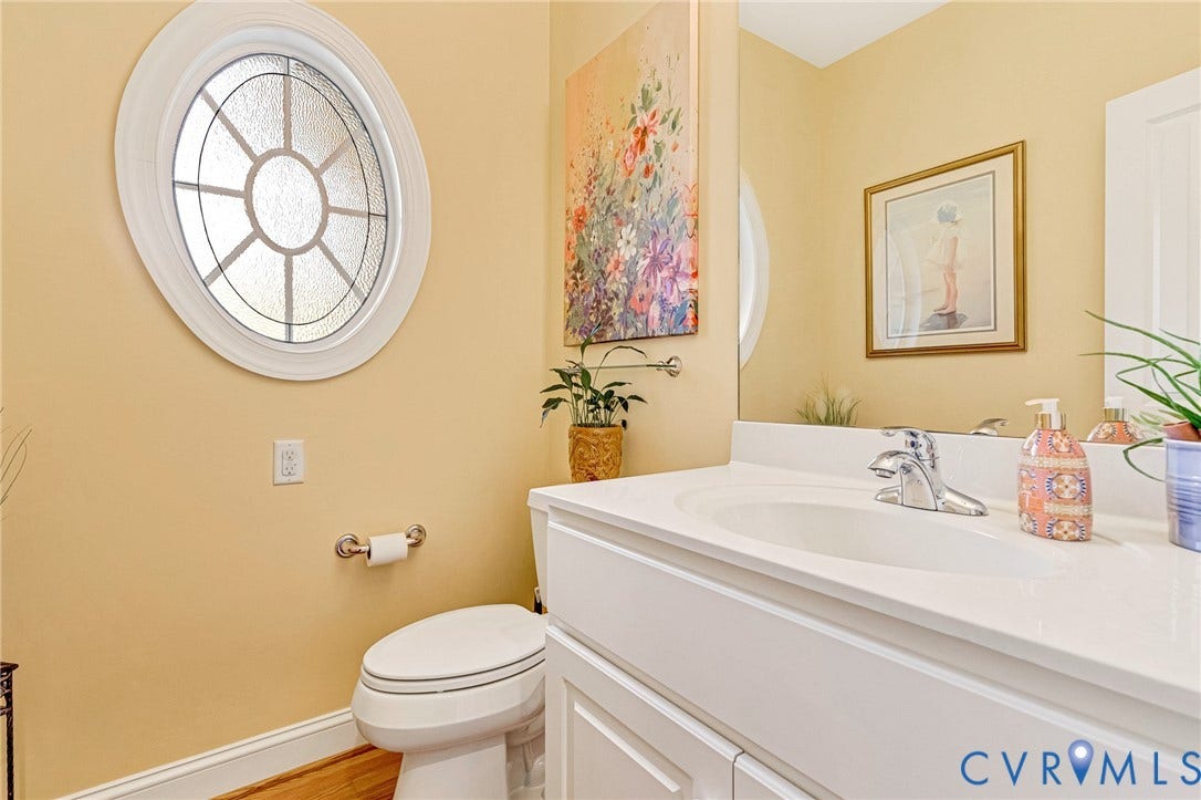 Oval decorative window, white vanity with integrated sink, chrome faucet, wall-mounted mirror, and wood-finish flooring