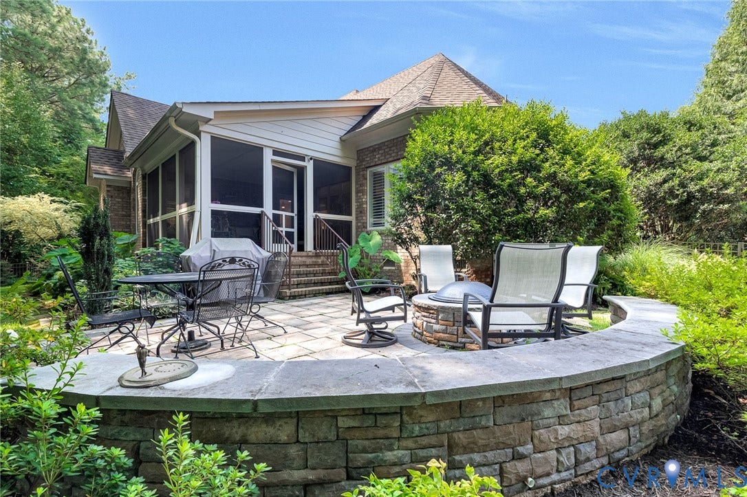 Expansive paver patio with a stone-clad fire pit, integrated stone retaining wall, and screened porch access