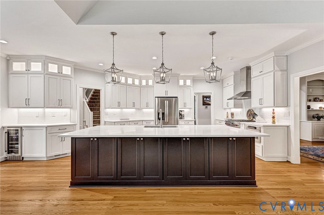 Expansive kitchen featuring a large central island with seating, white shaker cabinetry, stainless steel appliances, and wood-finish flooring