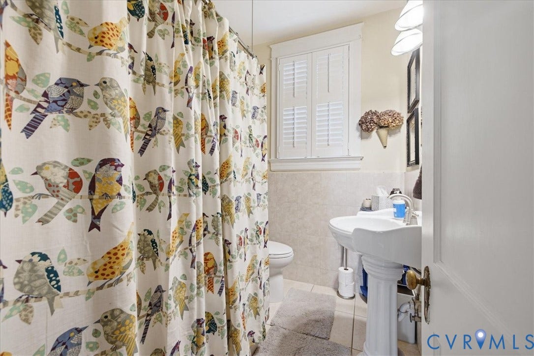 4702 New Kent Avenue, Westover Hills, Richmond, VA 23225 Main floor bath with white pedestal sink, chrome fixtures, tile flooring, window with white louvered shutters, and wall-mounted lighting