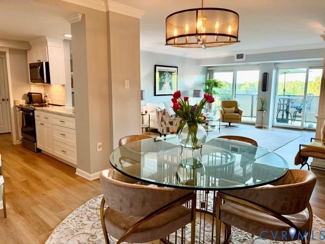 Open-concept living area featuring wood-finish flooring, a contemporary chandelier, white kitchen cabinetry with stainless steel appliances, and sliding glass doors opening to a balcony