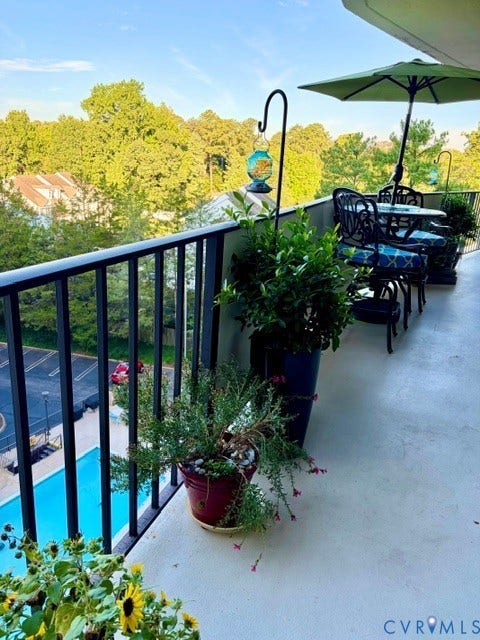 Spacious balcony with black iron railing, concrete flooring, and an amenity pool visible below