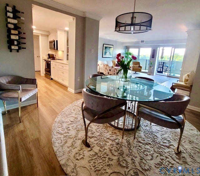 Open-concept living space with wood-finish flooring, a contemporary chandelier, and a kitchen featuring white cabinetry and stainless steel appliances