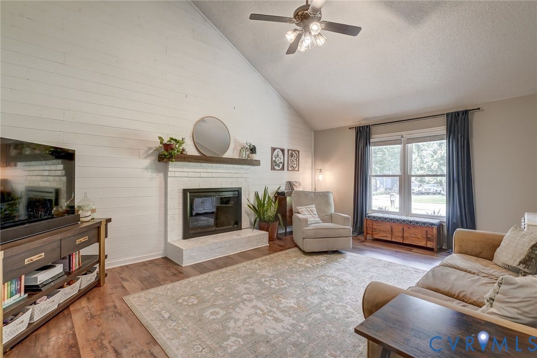 4647 Brookridge Road, Chesterfield, VA 23832 Vaulted ceiling with a ceiling fan, white shiplap accent wall, brick fireplace with a wood-finish mantel, and wood-finish flooring