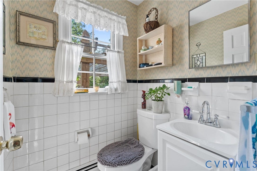 10205 Gwynnbrook Road, Richmond, VA 23235 White tiled walls with a black accent border, pedestal sink with chrome faucet, and a wall-mounted mirror