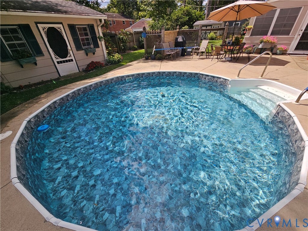 10205 Gwynnbrook Road, Richmond, VA 23235 Oval-shaped pool with integrated steps, concrete surround, and adjacent shed with shuttered windows
