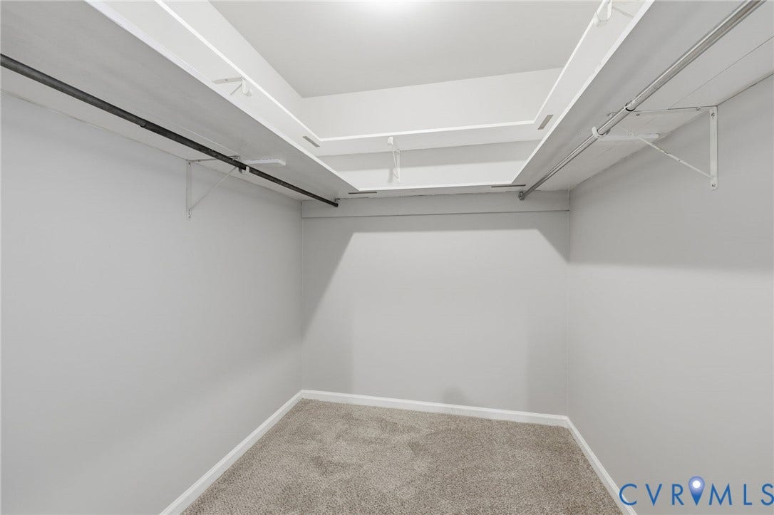 Walk-in storage space featuring neutral carpeting, tiered shelving, and dual metal clothing rods