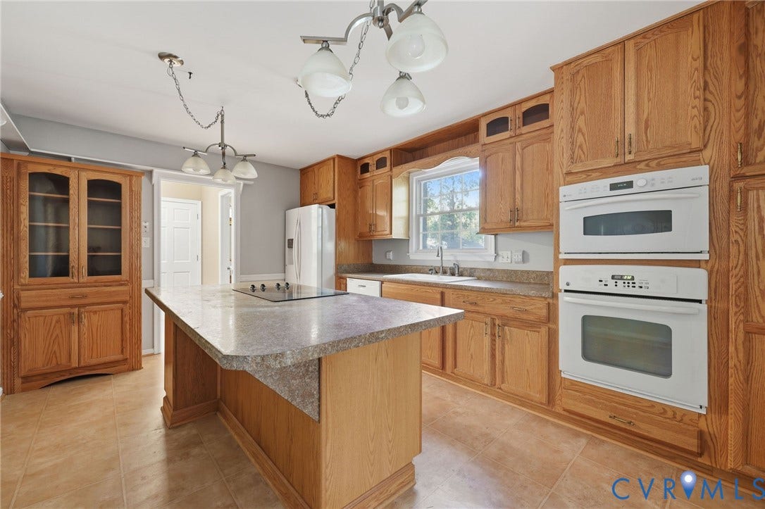 Kitchen featuring oak cabinetry, stone-finish countertops, a central island with a cooktop, double wall ovens, and tile flooring
