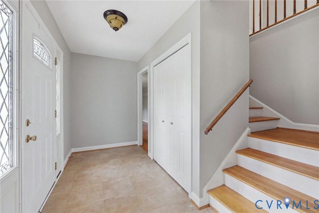 Foyer featuring tile flooring, a door with a decorative glass insert, built-in closet cabinetry, and a staircase with wood-finish treads and a wood handrail