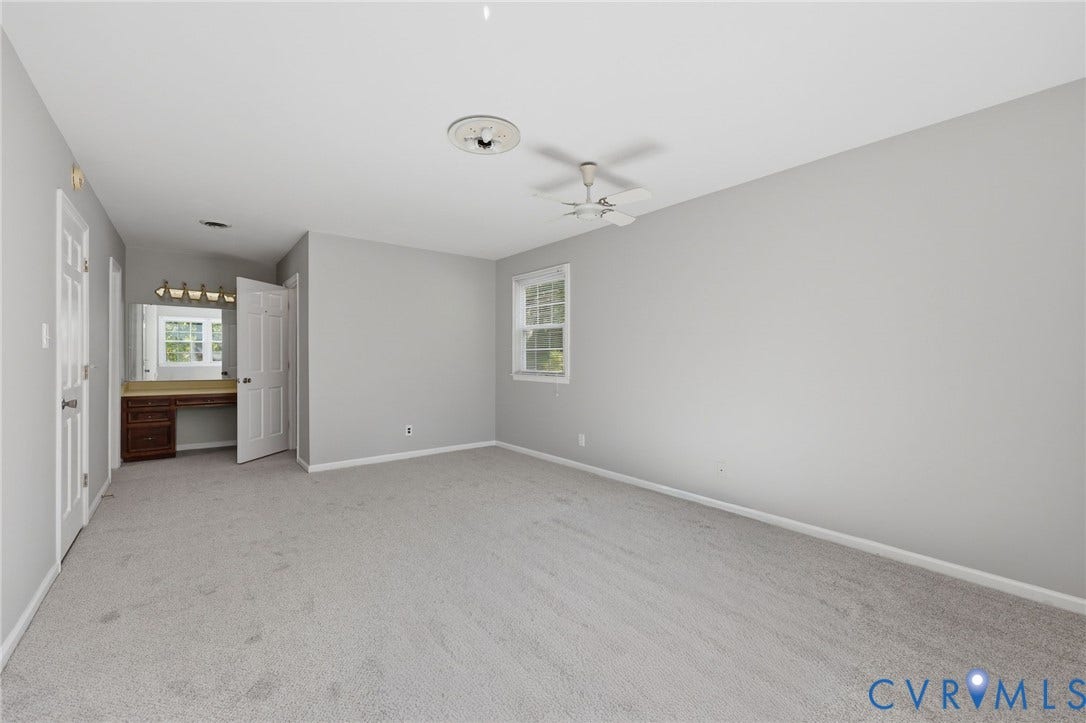 Neutral-toned carpeted flooring, built-in vanity with wood-finish cabinetry, multi-blade ceiling fan, and window with white trim