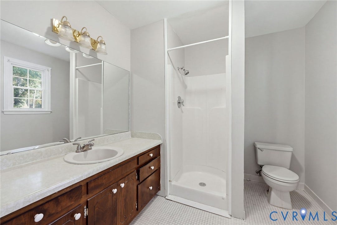 Bathroom featuring a wood-finish vanity with a stone-composite countertop, oval drop-in sink, glass-paneled shower enclosure, and mosaic floor tiling