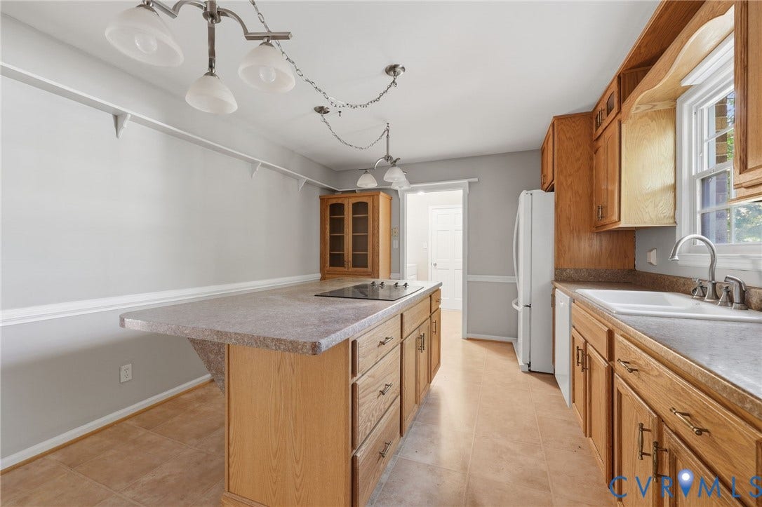 Kitchen featuring wood cabinetry, integrated island with a cooktop, double-basin sink, and multi-pendant lighting
