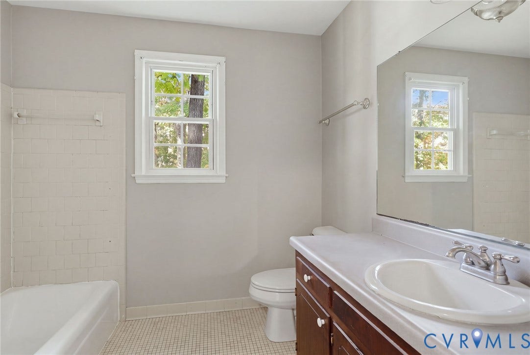 Bathroom featuring a white tub with tiled surround, a dark wood vanity with an integrated sink, a large wall-mounted mirror, and tile flooring