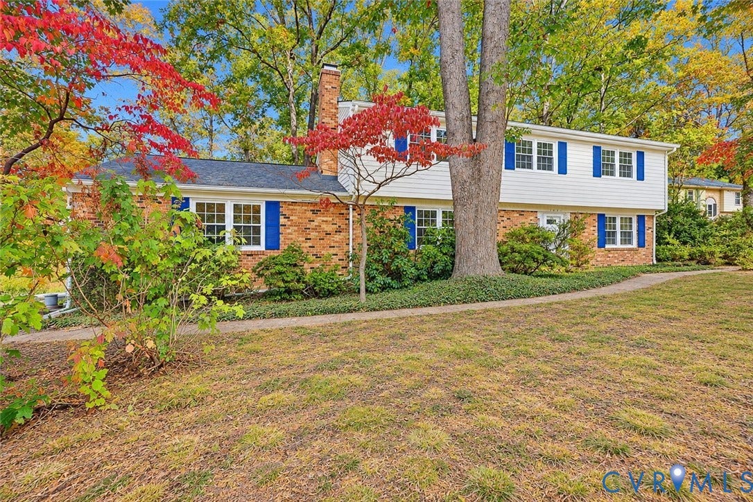 Two-story residence featuring a brick and horizontal siding exterior, blue window shutters, shingled roof, and a central brick chimney